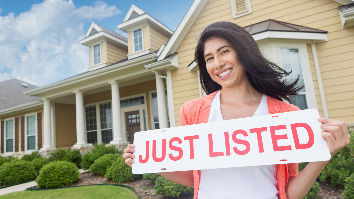 Smiling female holding just listed sign in front of beautiful house