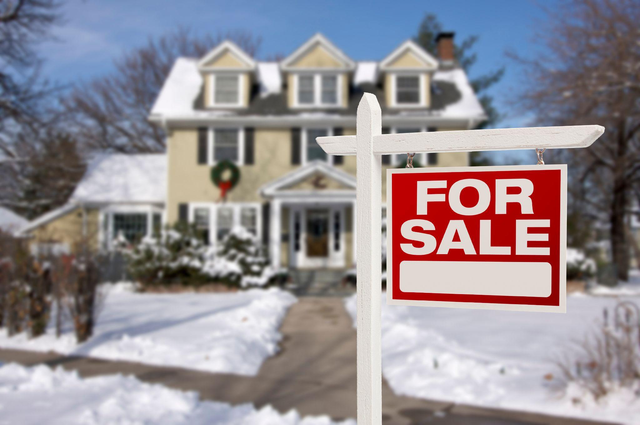 Home for sale sign in front of snowy new house