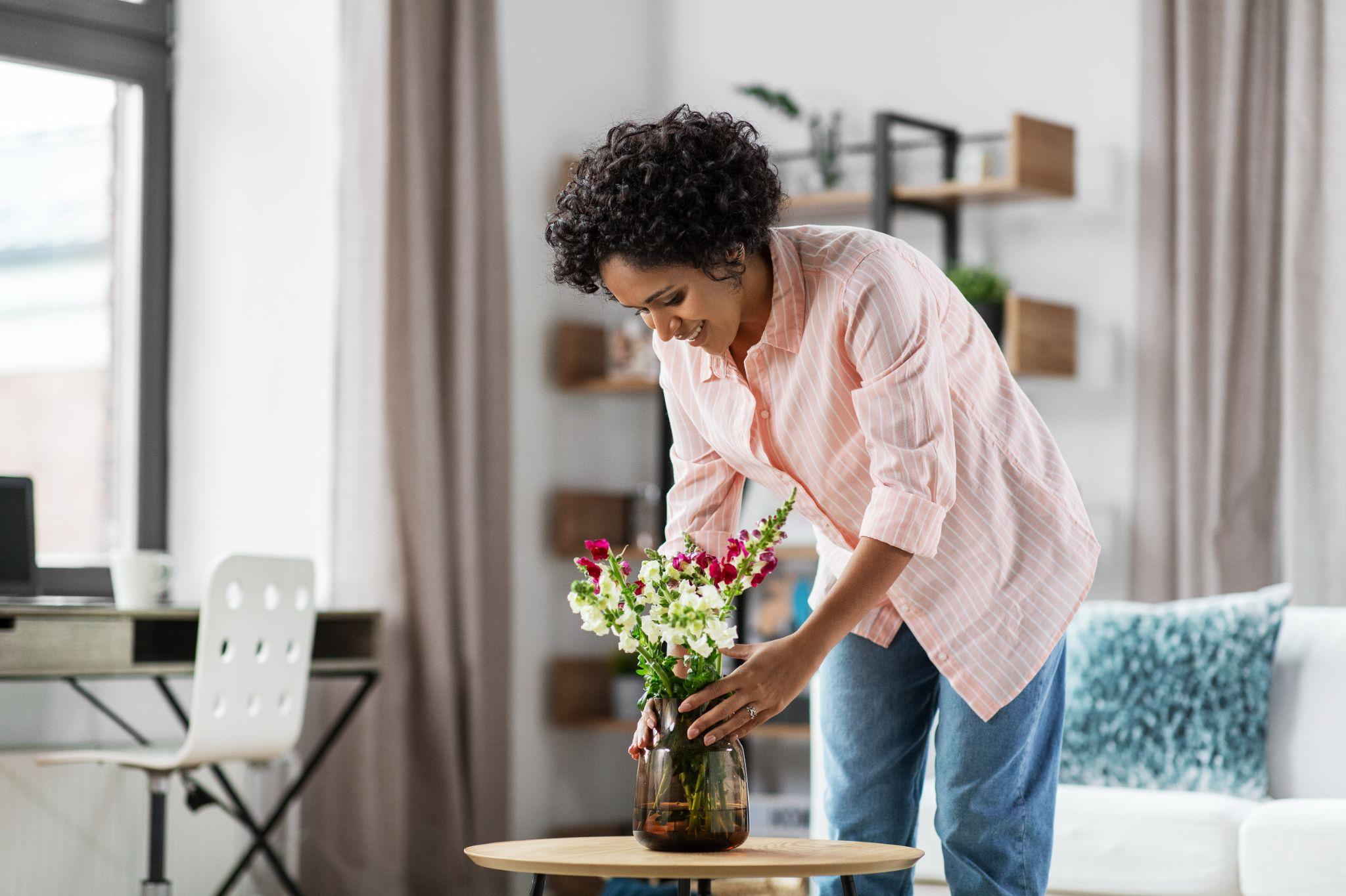 happy smiling young woman placing flowers on coffee table