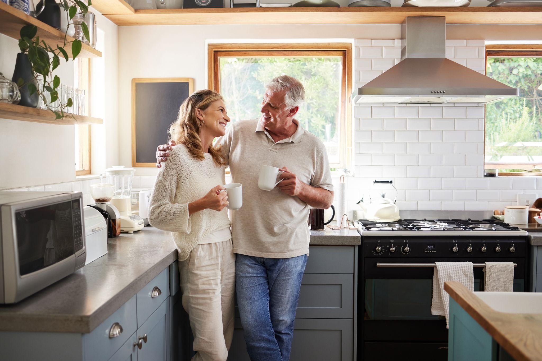 Older couple in their kitchen having a conversation over coffee.