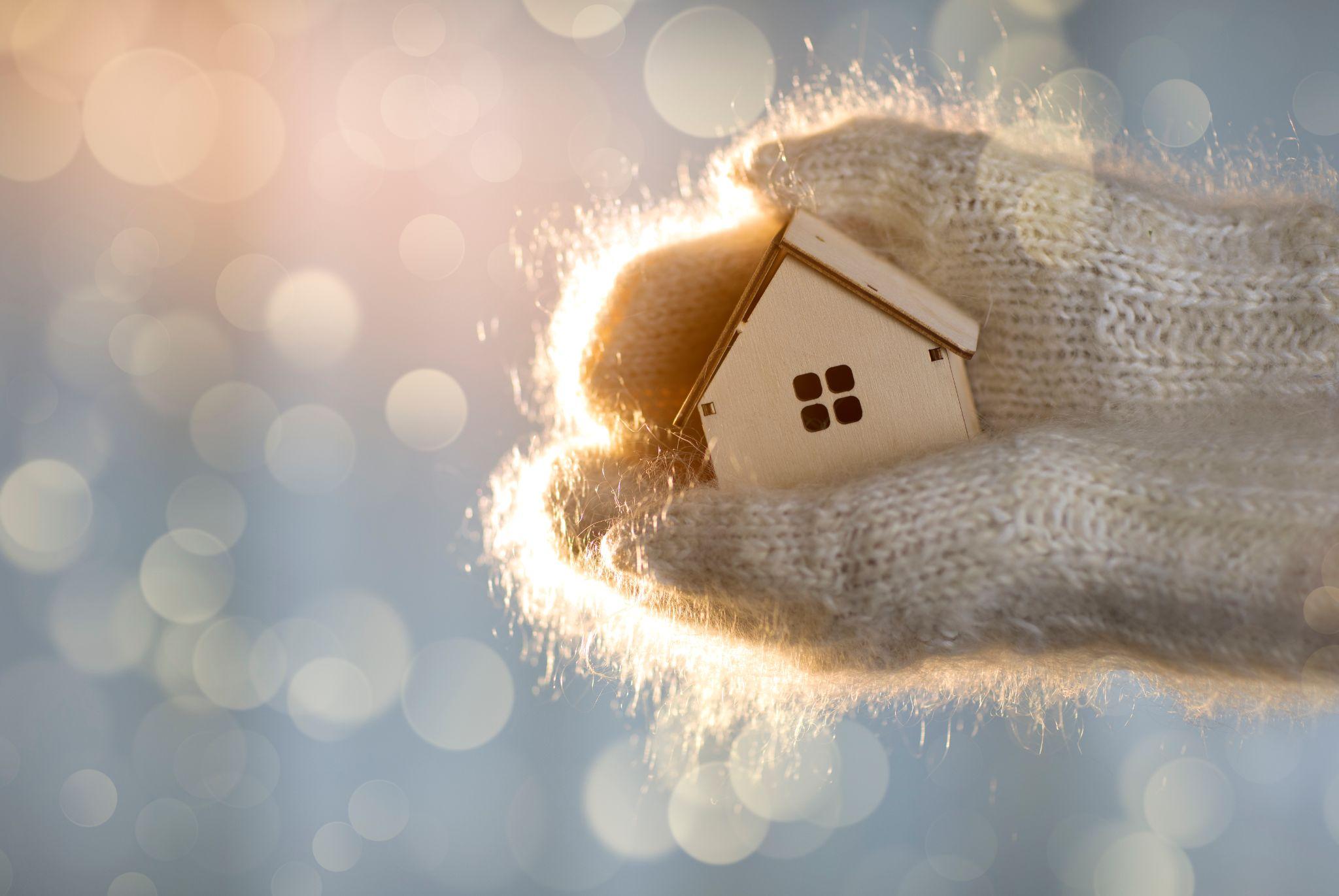 Gloves holding a small house model with snow falling behind