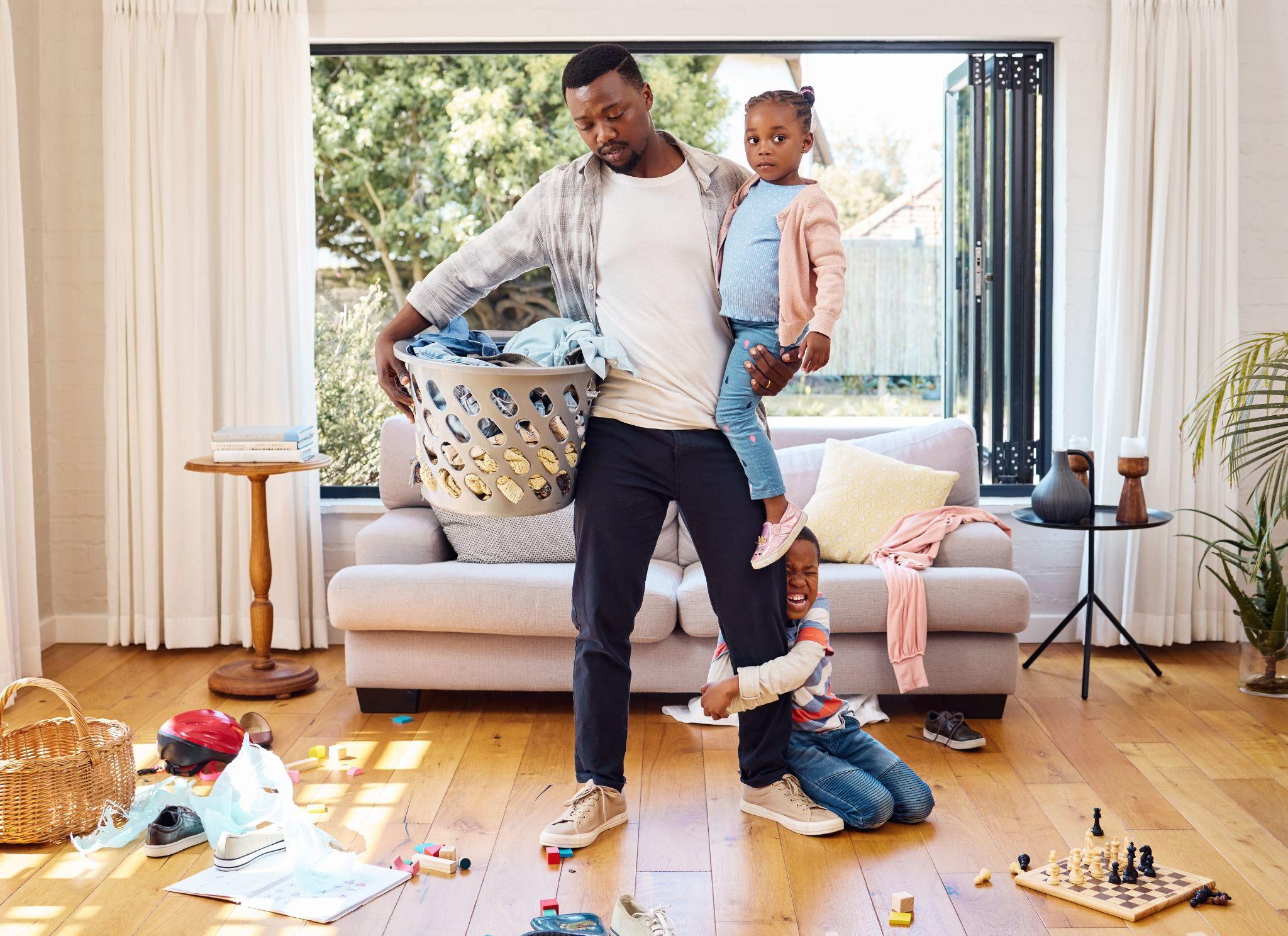 A dad holding his daughter standing in a messy room