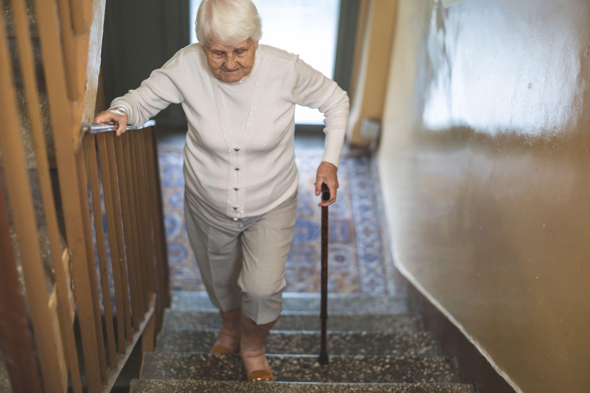An older woman with a cane walking up stairs