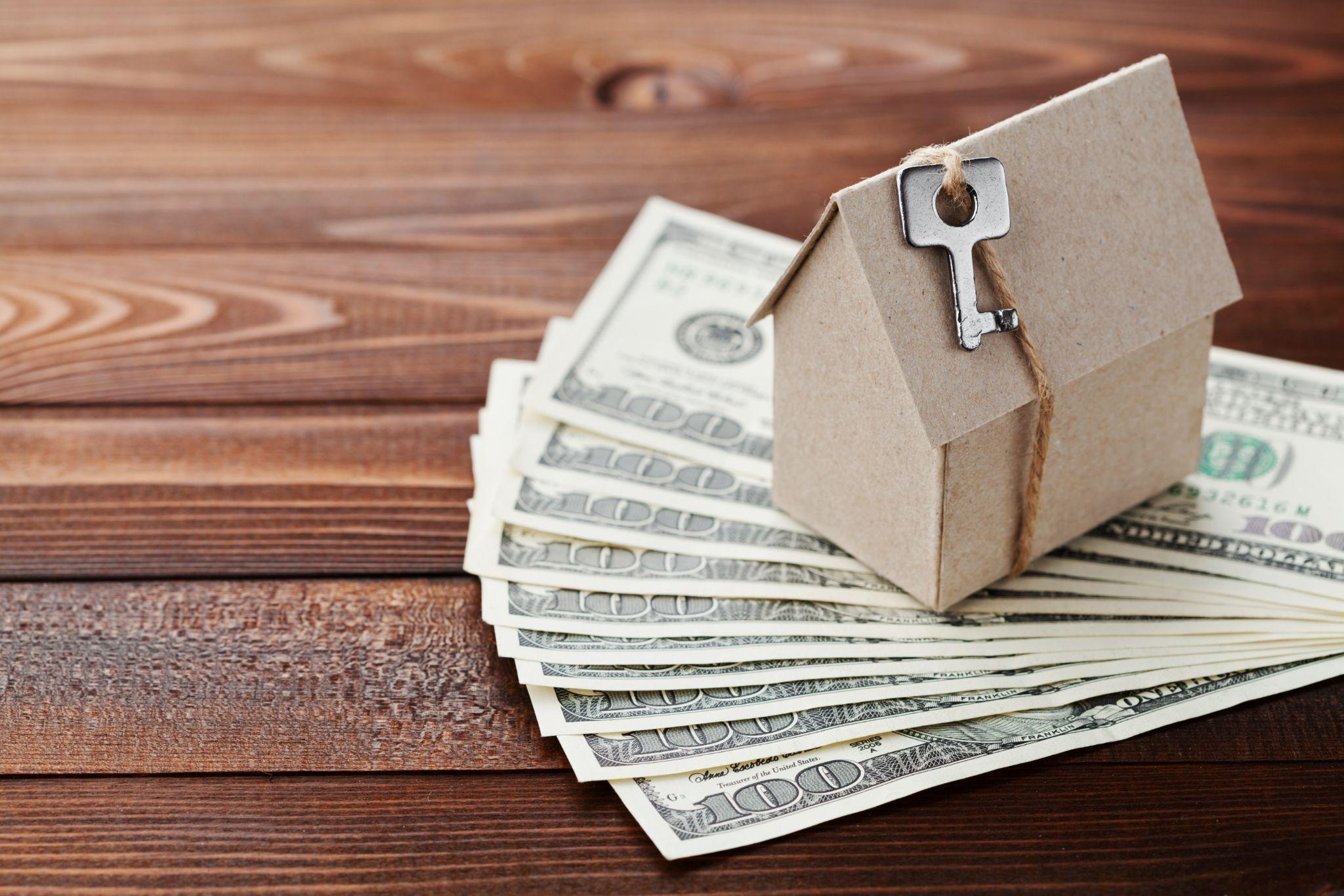 Cardboard house with key and dollar money. Building, insurance, housewarming, loan, real estate, cost of housing or buying a new home concept.