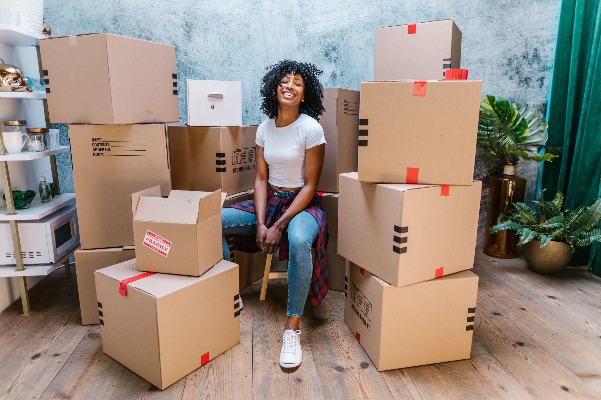 Happy Woman Sitting Against Stacked Cardboard Boxes
