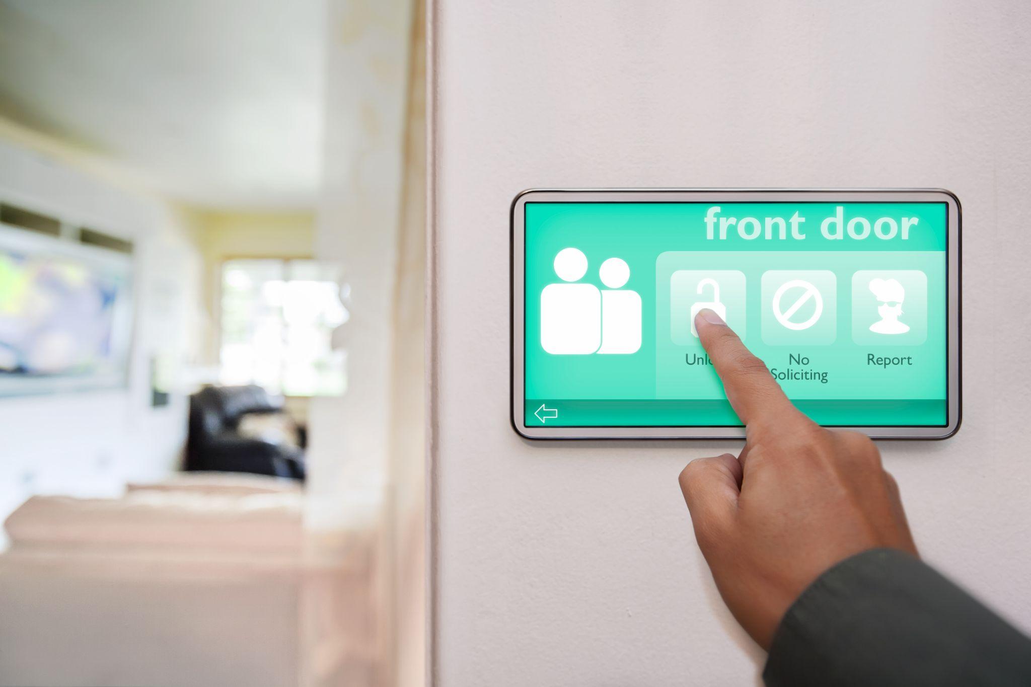 Home owner unlocking the front door of home, using a touchscreen device to control all the connected smart home features.