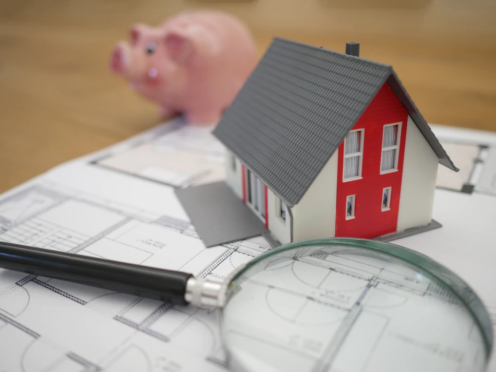 model of a house next to a magnifying glass on blueprints