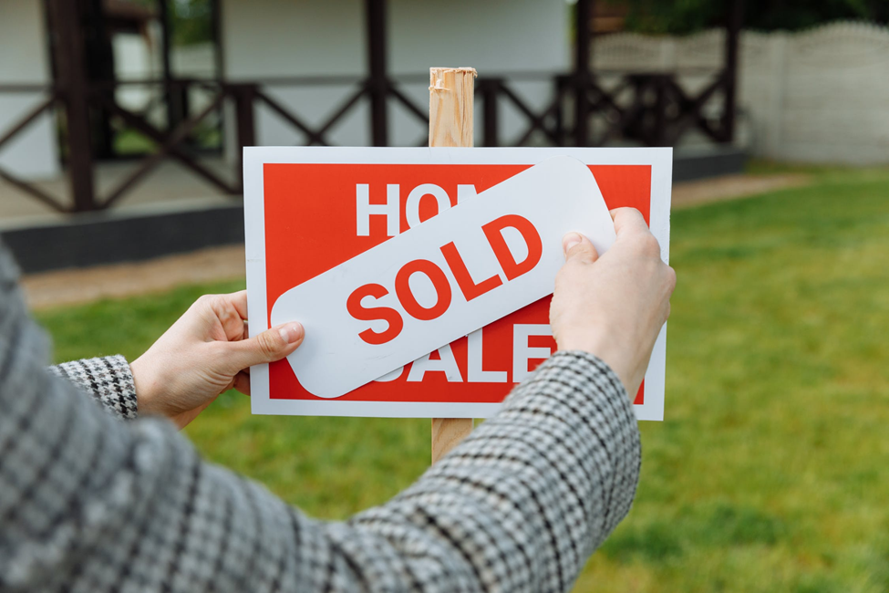 man placing a sold sticker on a house for sale sign