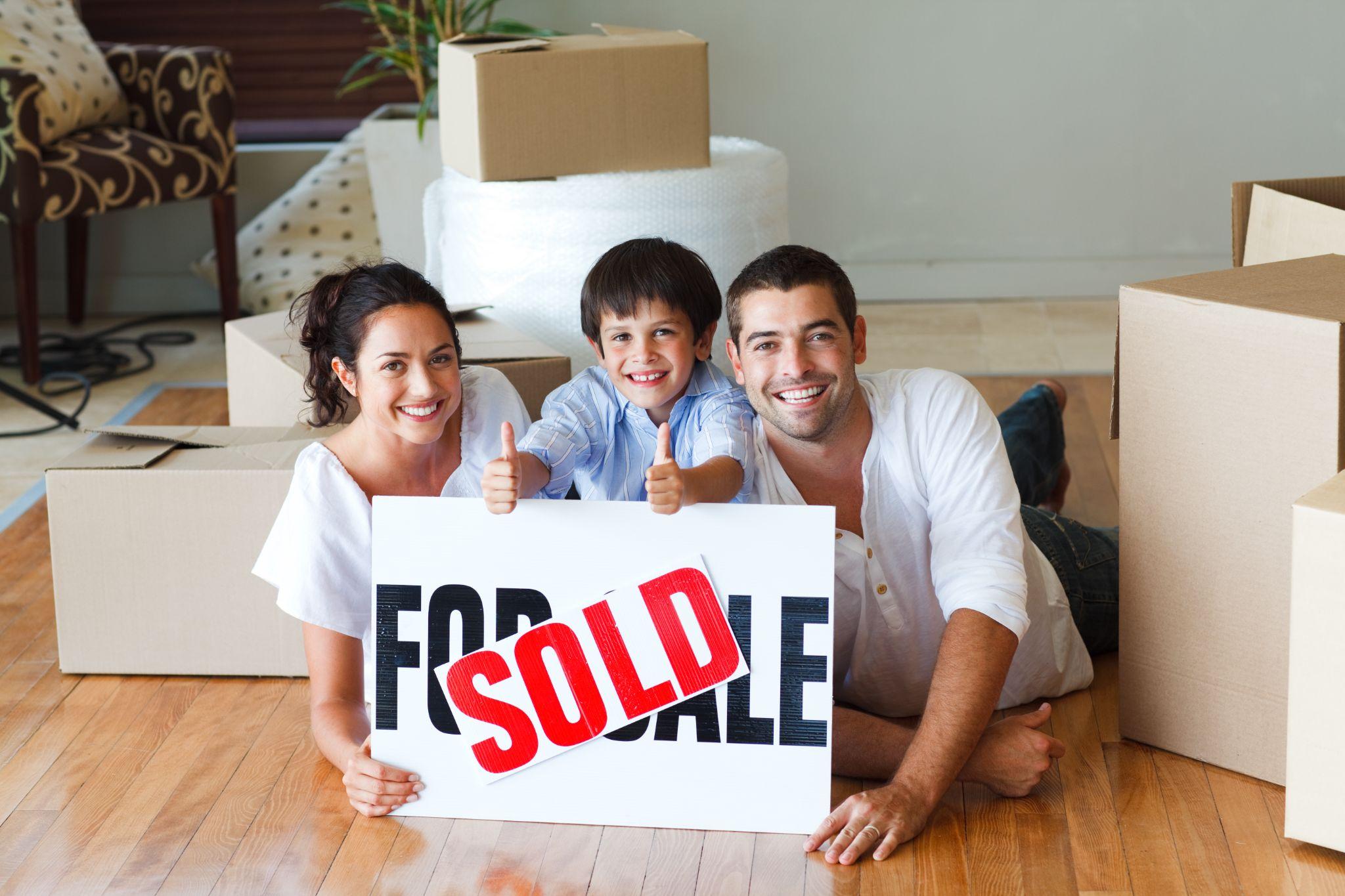 Small family holding up a sold home sign