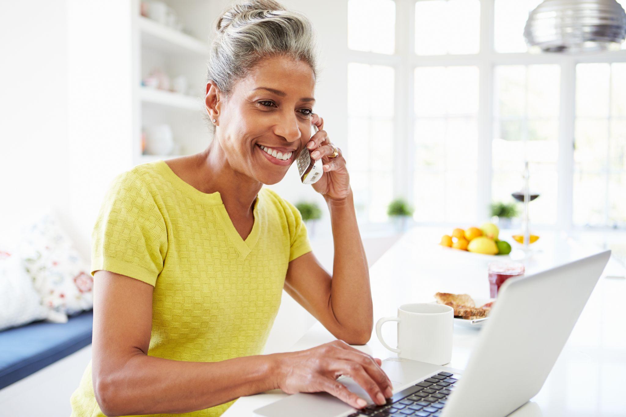 Woman using laptop and talking on phone at home