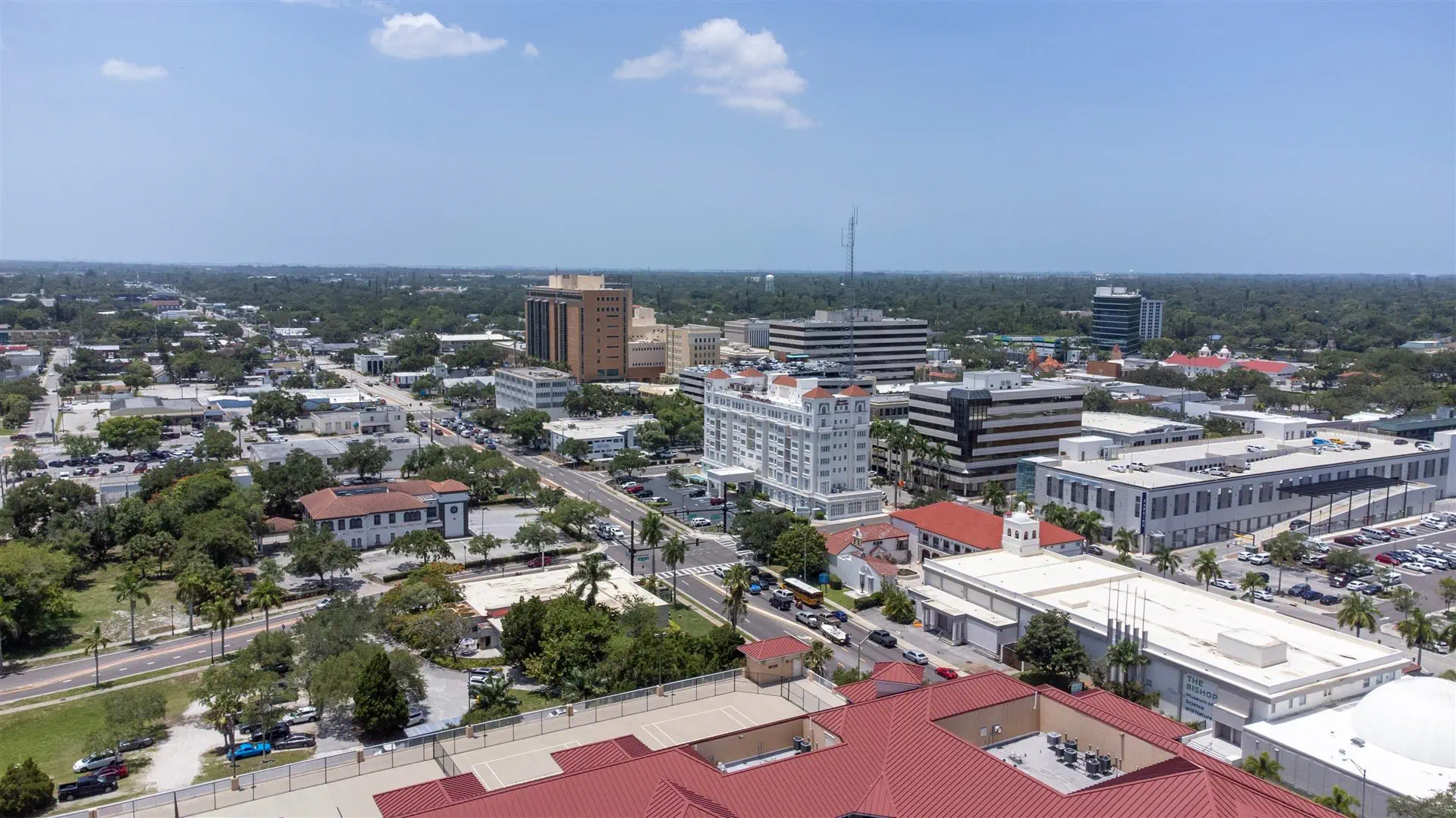 Aerial view of a cityscape with a mix of modern and historic buildings, lush green spaces, and a clear blue sky, conveying a serene urban atmosphere.