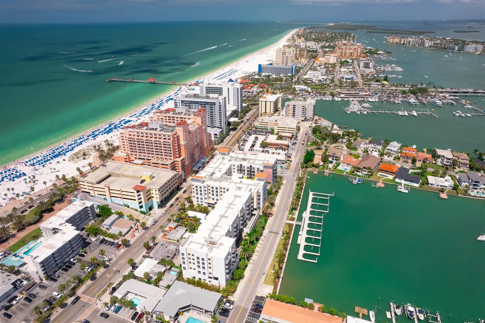 Aerial view of a vibrant coastal cityscape with high-rise hotels, a bustling marina, and a stretch of white sandy beach along a turquoise sea.