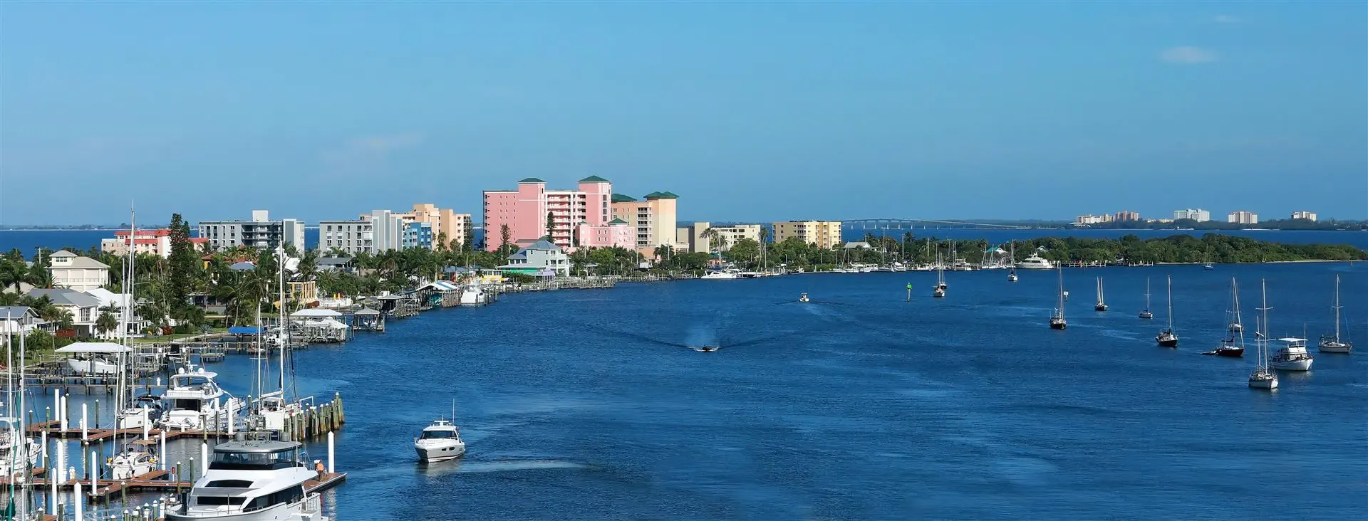 Coastal cityscape with vibrant blue water, sailboats, and yachts. Colorful buildings line the shore, evoking a relaxed, sunny seaside ambiance.