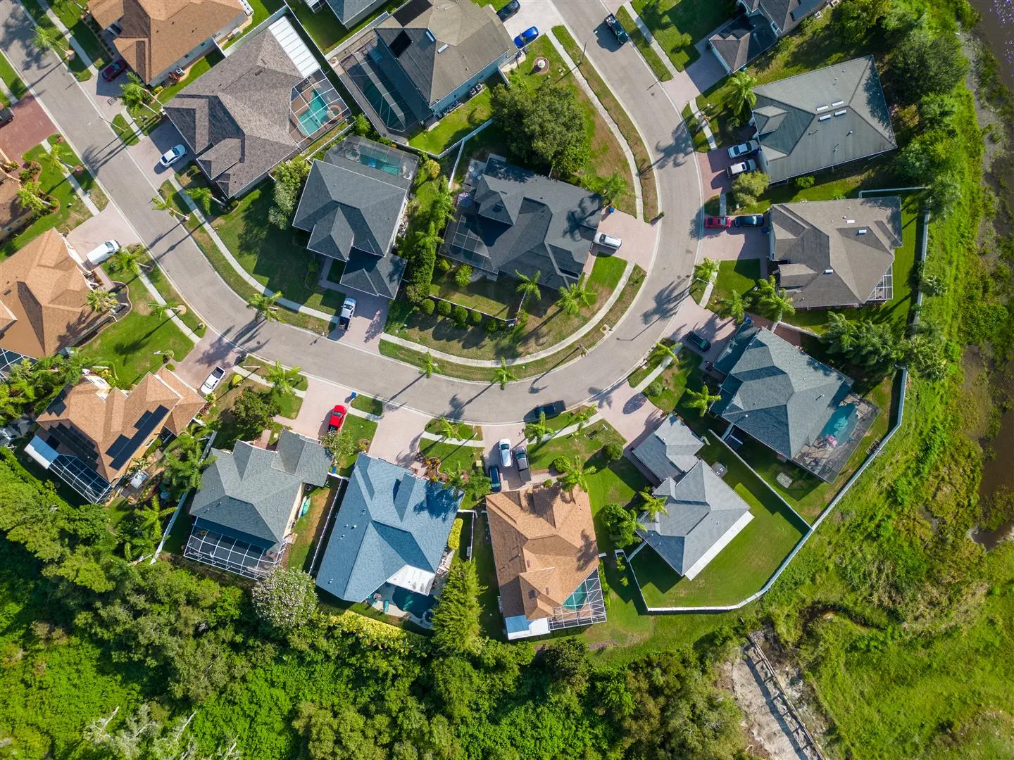 Aerial view of a suburban neighborhood with houses arranged on a curved street. Lush greenery and lawns surround the homes, creating a peaceful atmosphere.
