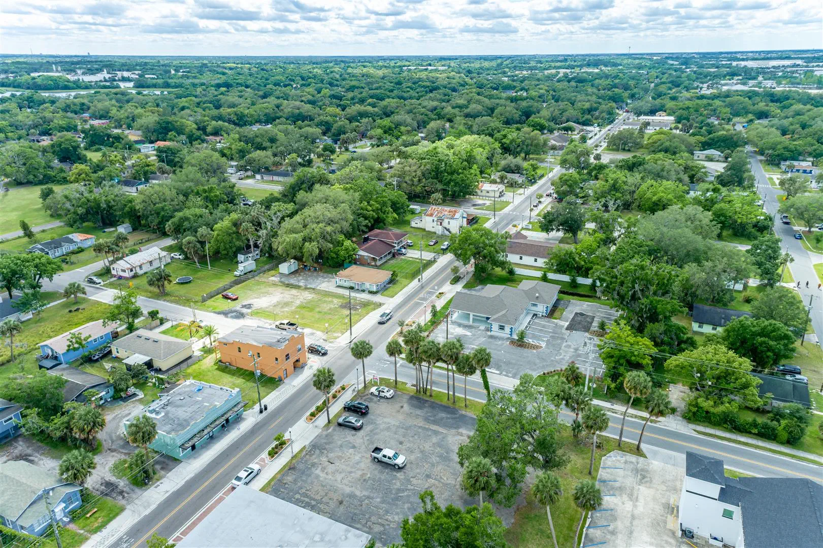 Aerial view of a lush, green suburban neighborhood with tree-lined streets, colorful houses, a few parked cars, and clear skies above, conveying tranquility.