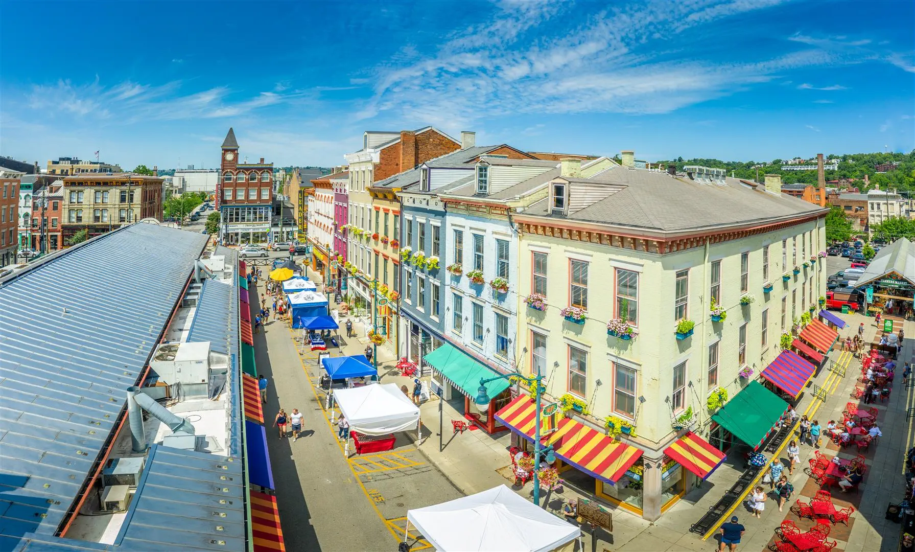 A vibrant street market with colorful vendor tents lines a bustling street. Historic buildings with flower-adorned balconies create a lively, festive atmosphere.