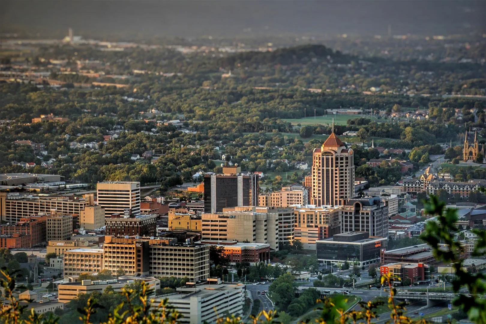 Aerial view of a cityscape at dusk, showcasing a mix of modern high-rise and older buildings surrounded by lush greenery, conveying a peaceful urban ambiance.